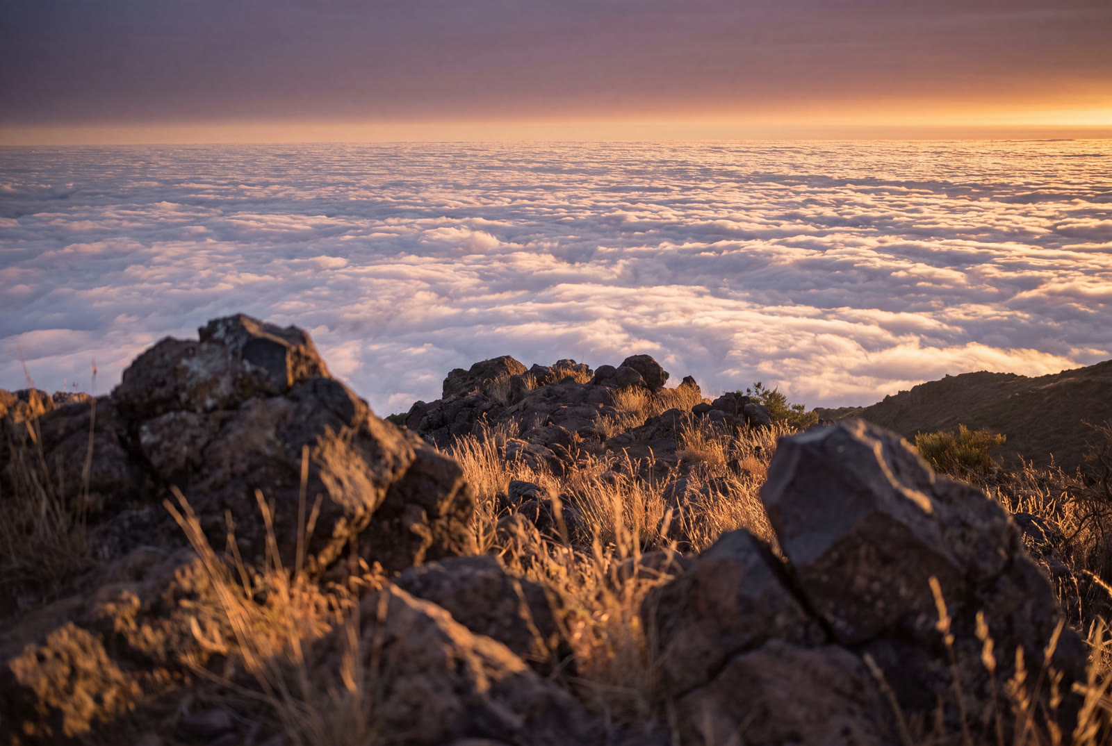 Weiter Blick von einem Vulkangrat über ein leuchtendes Wolkenmeer bis zum klaren Horizont